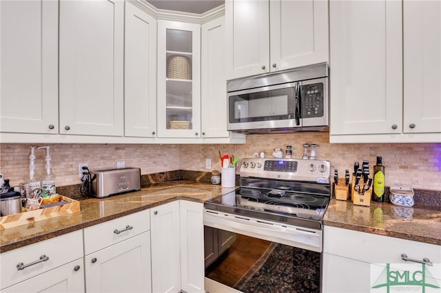 kitchen featuring white cabinets, decorative backsplash, stainless steel appliances, and dark stone countertops