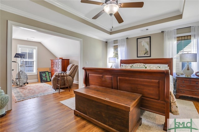 bedroom with ceiling fan, a raised ceiling, wood-type flooring, and crown molding