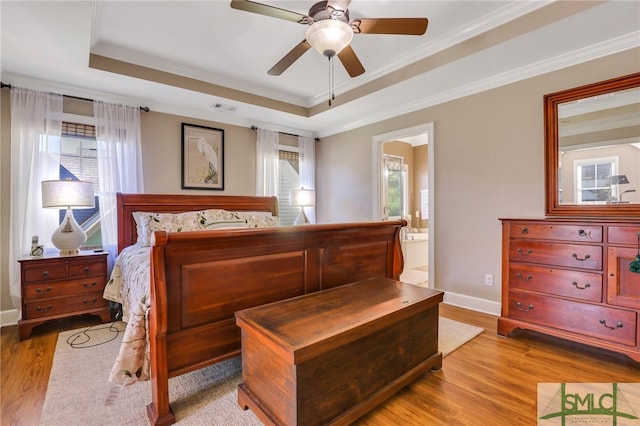 bedroom featuring a raised ceiling, crown molding, ceiling fan, light wood-type flooring, and connected bathroom