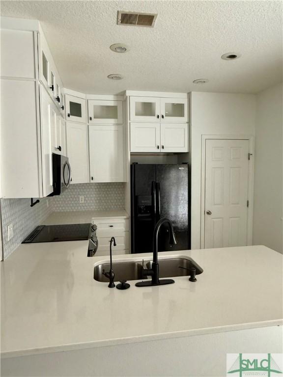 kitchen with sink, backsplash, white cabinets, and black fridge with ice dispenser