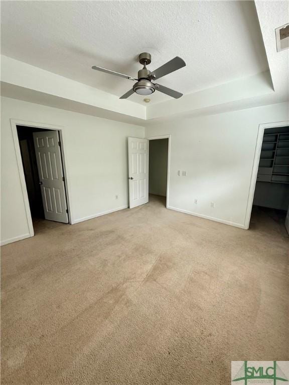 spare room featuring light carpet, ceiling fan, a textured ceiling, and a tray ceiling