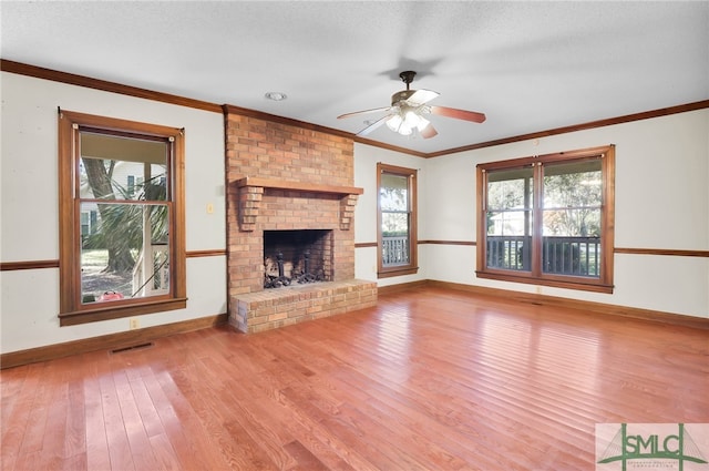 unfurnished living room with ornamental molding, a textured ceiling, ceiling fan, light hardwood / wood-style flooring, and a fireplace