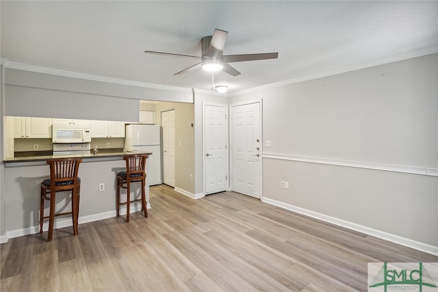 kitchen with white appliances, light hardwood / wood-style flooring, ornamental molding, a kitchen bar, and kitchen peninsula