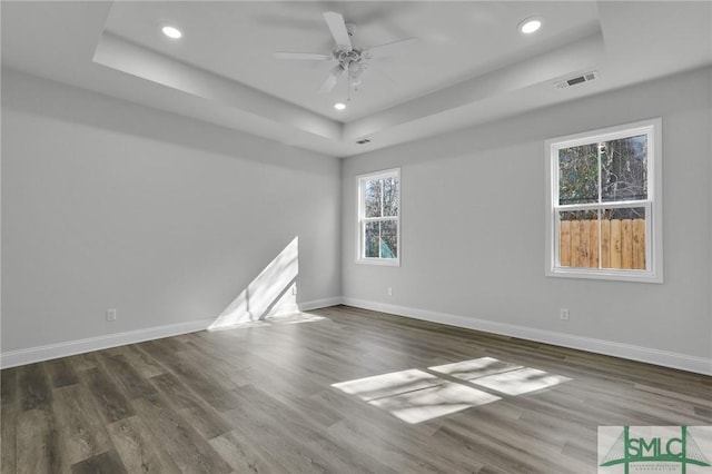 unfurnished room with a tray ceiling, dark wood-type flooring, and ceiling fan