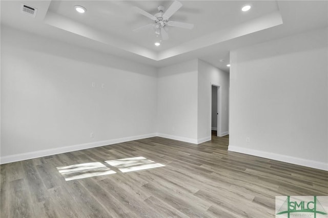 empty room with a raised ceiling, wood-type flooring, and ceiling fan