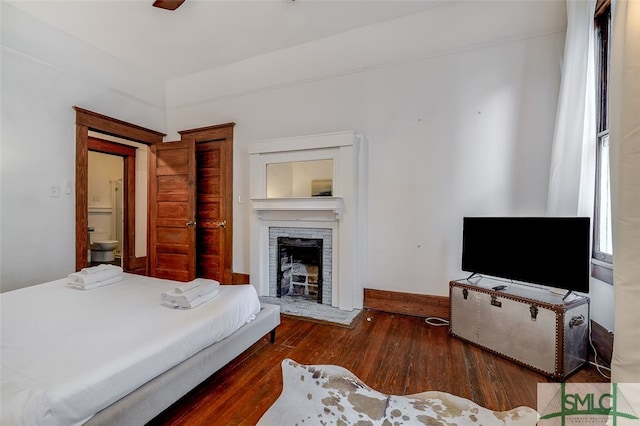 bedroom featuring ceiling fan, a fireplace, ensuite bathroom, and dark wood-type flooring