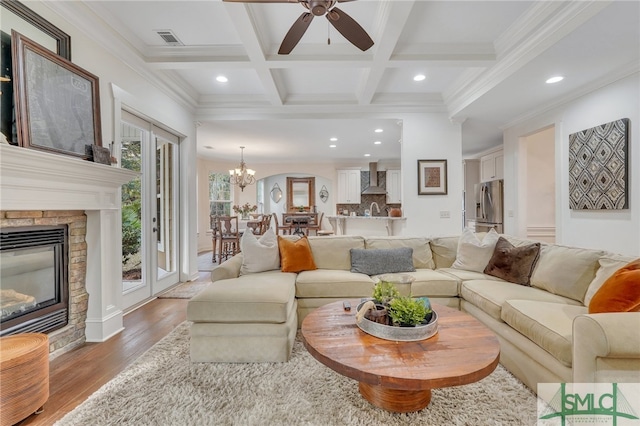 living room with a brick fireplace, coffered ceiling, ceiling fan with notable chandelier, beam ceiling, and hardwood / wood-style flooring