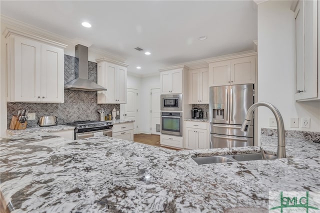 kitchen with light stone counters, white cabinets, stainless steel appliances, and wall chimney range hood