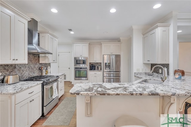 kitchen featuring a breakfast bar, sink, wall chimney exhaust hood, light stone countertops, and stainless steel appliances