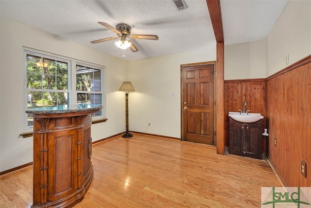 interior space featuring sink, wooden walls, ceiling fan, light wood-type flooring, and a textured ceiling