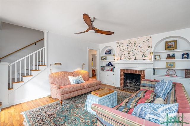 living room featuring built in shelves, ceiling fan, a fireplace, and hardwood / wood-style flooring