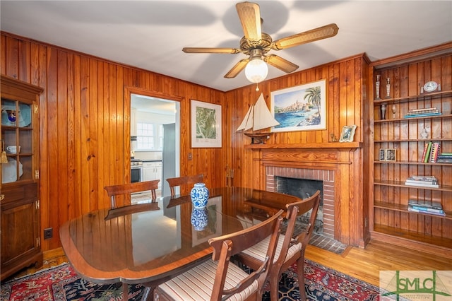 dining room with ceiling fan, a brick fireplace, light hardwood / wood-style flooring, built in features, and wooden walls