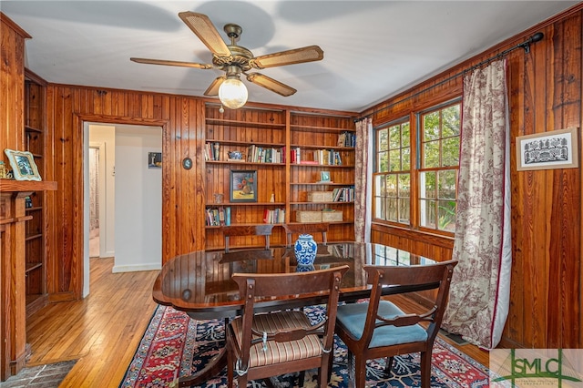 dining space with ceiling fan, light hardwood / wood-style floors, wooden walls, and built in shelves