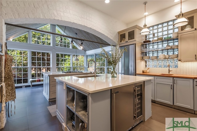 kitchen featuring decorative backsplash, sink, pendant lighting, lofted ceiling, and an island with sink