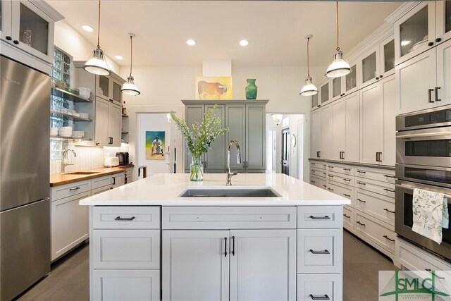 kitchen with appliances with stainless steel finishes, a center island with sink, hanging light fixtures, and sink