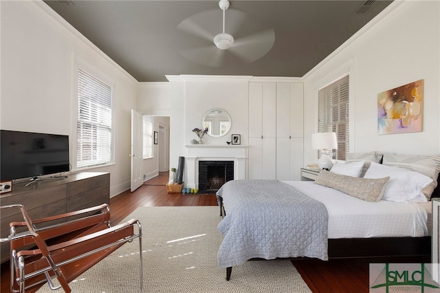 bedroom featuring visible vents, wood finished floors, a fireplace with flush hearth, and ornamental molding