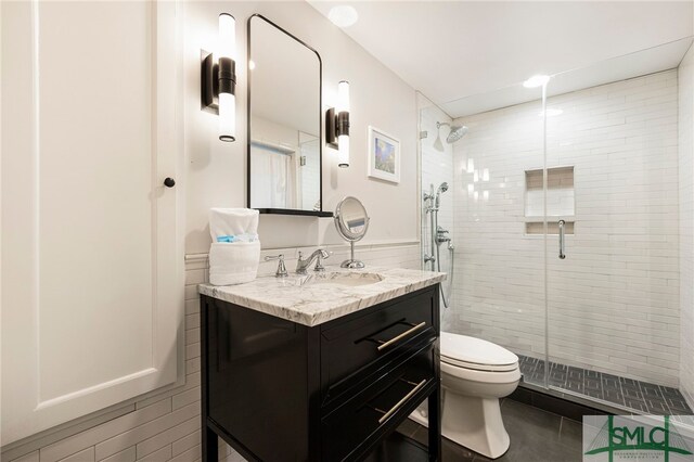 bathroom featuring vanity, toilet, a shower with door, and tile walls