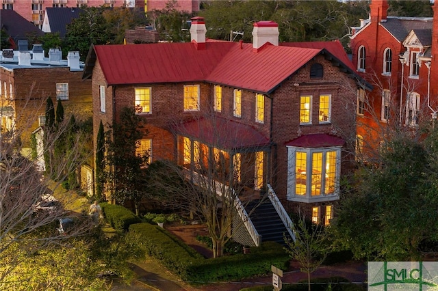 view of front of property featuring stairway, metal roof, brick siding, and a chimney