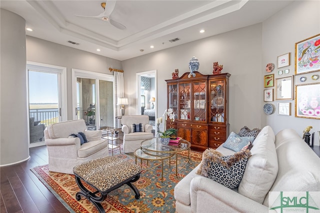 living room with a raised ceiling, ceiling fan, and dark wood-type flooring