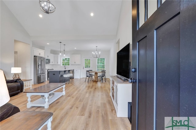 living room with light hardwood / wood-style floors, sink, high vaulted ceiling, and a chandelier