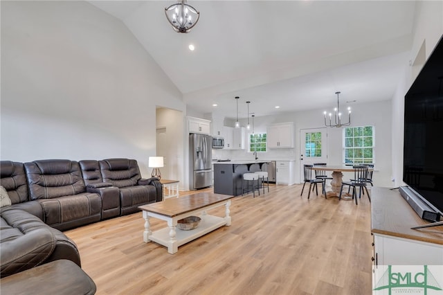 living room with an inviting chandelier, light hardwood / wood-style flooring, and lofted ceiling