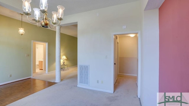 empty room with ornate columns, light carpet, a chandelier, and a textured ceiling