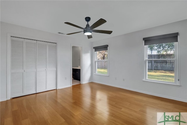 unfurnished bedroom featuring ceiling fan, ensuite bath, light hardwood / wood-style flooring, and multiple windows