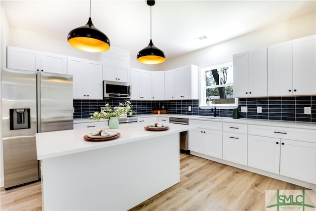 kitchen with appliances with stainless steel finishes, backsplash, pendant lighting, a center island, and white cabinetry