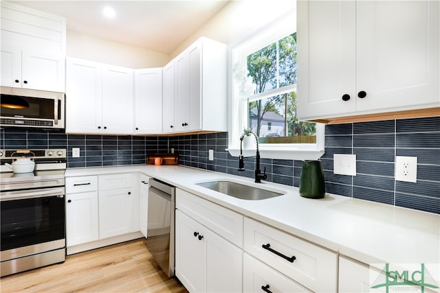 kitchen featuring white cabinetry, sink, backsplash, light hardwood / wood-style floors, and appliances with stainless steel finishes