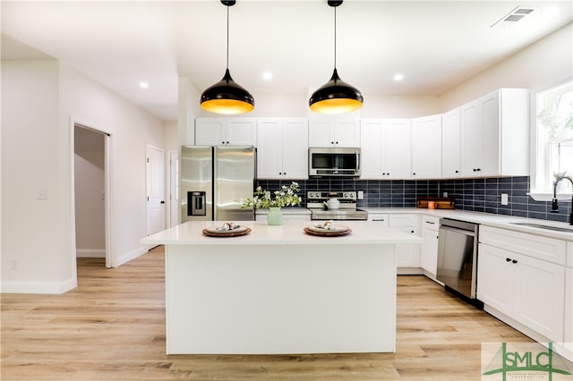 kitchen with appliances with stainless steel finishes, light wood-type flooring, sink, white cabinets, and a kitchen island