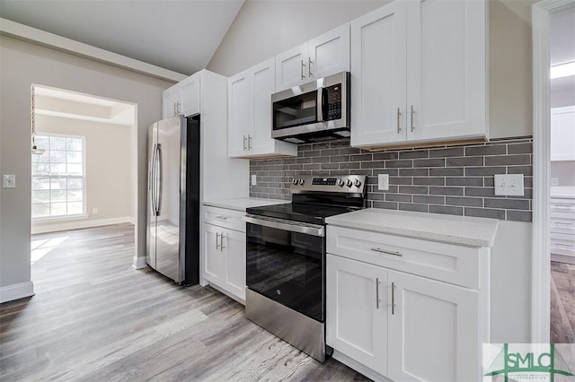 kitchen featuring white cabinets, light wood-type flooring, stainless steel appliances, and lofted ceiling