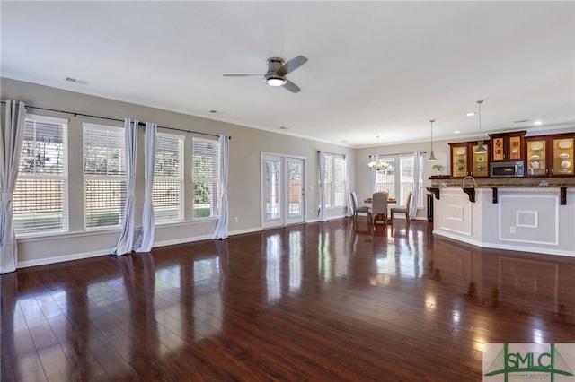 unfurnished living room with plenty of natural light, ceiling fan with notable chandelier, and dark hardwood / wood-style floors