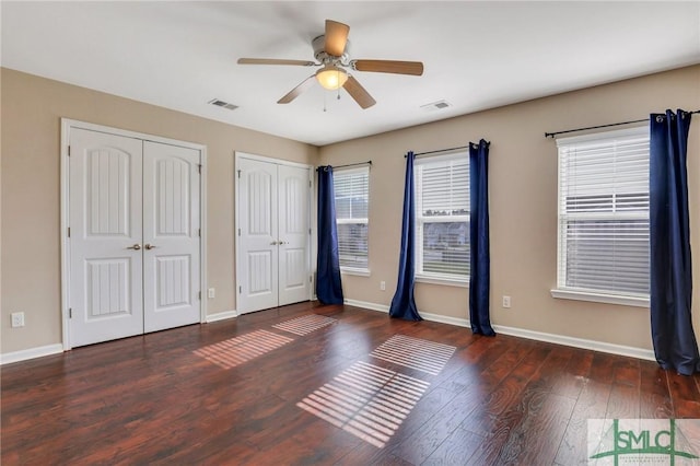 unfurnished bedroom featuring multiple closets, ceiling fan, and dark hardwood / wood-style flooring