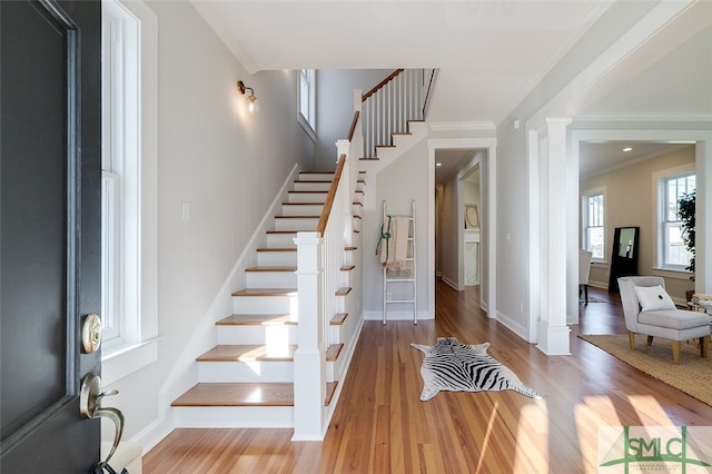 foyer entrance with wood-type flooring, ornate columns, and crown molding