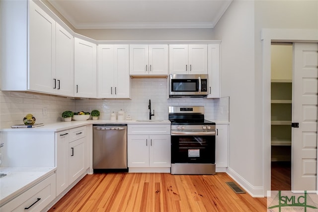 kitchen featuring tasteful backsplash, white cabinetry, light hardwood / wood-style flooring, and appliances with stainless steel finishes