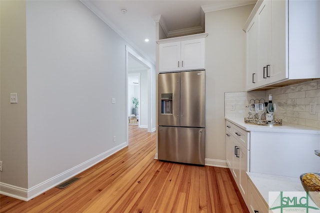 kitchen featuring decorative backsplash, stainless steel refrigerator with ice dispenser, light wood-type flooring, ornamental molding, and white cabinets