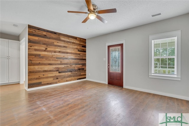 entrance foyer featuring wood walls, ceiling fan, light hardwood / wood-style floors, and a textured ceiling