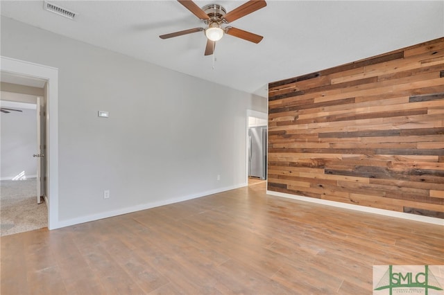 spare room featuring hardwood / wood-style floors, ceiling fan, and wooden walls