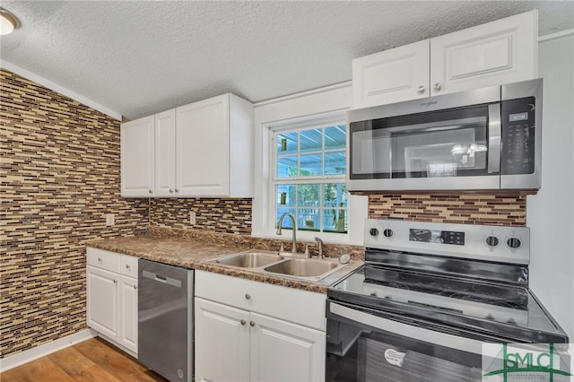 kitchen with wood-type flooring, stainless steel appliances, white cabinetry, and sink