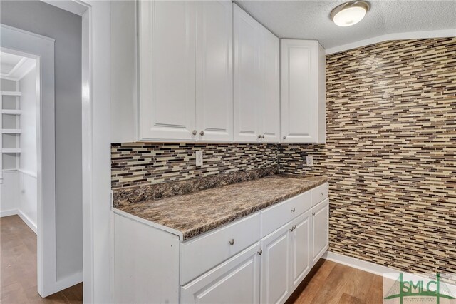 bar with decorative backsplash, a textured ceiling, vaulted ceiling, white cabinets, and light hardwood / wood-style floors