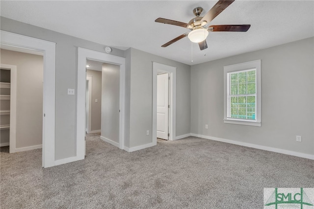 unfurnished bedroom with a closet, a walk in closet, light colored carpet, and ceiling fan