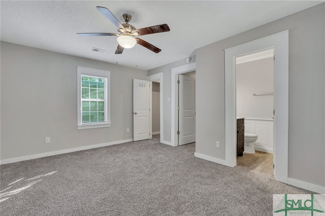 unfurnished bedroom featuring connected bathroom, ceiling fan, light colored carpet, and a textured ceiling