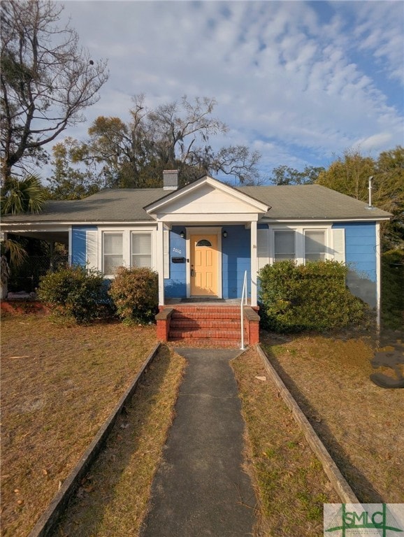 bungalow-style house with a chimney and a front yard