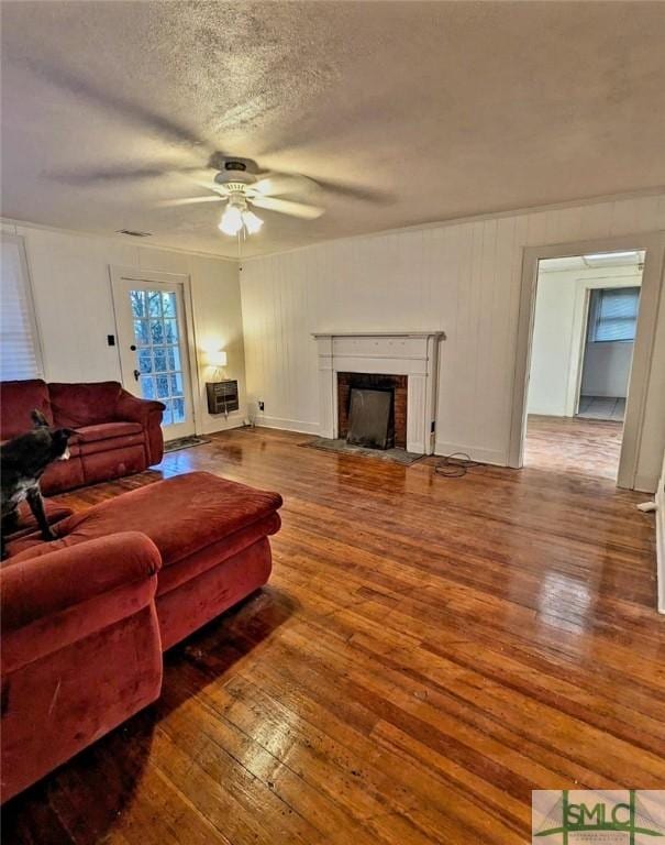 living room featuring hardwood / wood-style floors, ceiling fan, a fireplace, and a textured ceiling