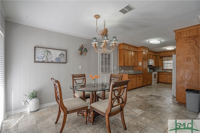 dining area featuring an inviting chandelier, wooden walls, and crown molding