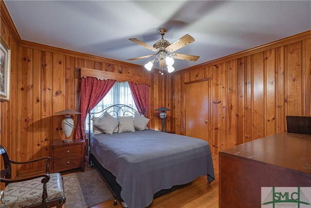 bedroom featuring ornamental molding, light hardwood / wood-style floors, ceiling fan, and wooden walls