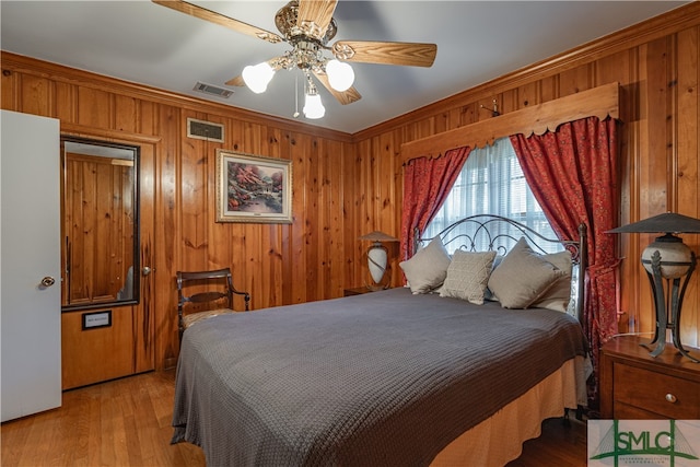 bedroom featuring ceiling fan, light hardwood / wood-style floors, crown molding, and wooden walls