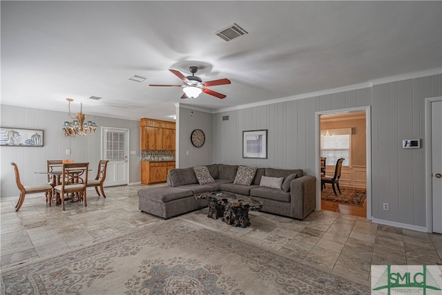 living room featuring ceiling fan with notable chandelier, wooden walls, and ornamental molding