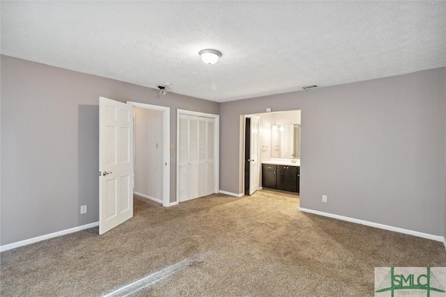 unfurnished bedroom featuring a textured ceiling, carpet floors, and ensuite bath