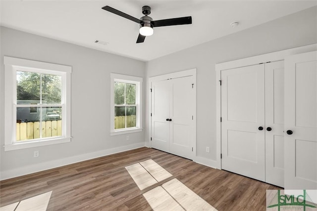 unfurnished bedroom with hardwood / wood-style flooring, ceiling fan, and multiple closets